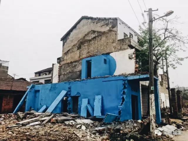 △ 這棟建筑是臨江最近的半拆遷建筑物的遺留，沅江和堤壩成為了展覽的天然背景。創(chuàng)作團隊對這棟建筑進行了半涂裝，將符號性的沅水曲線與拆遷進行中的建筑立面進行意義的疊造，它們共同觸發(fā)了場所空間多元語境的生成，把拆遷這種暫時破壞性、干擾性的介入行動與沅水右岸發(fā)展的未來性、美好性緊密融合。